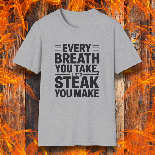 Sport Grey T-shirt with bold white text that reads "Every Breath You Take, Every Steak You Make," displayed over a rustic wood and flame background — a humorous grilling shirt perfect for steak fans.