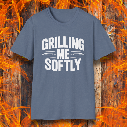 Heather Indigo T-shirt with bold white text that says "Grilling Me Softly," featuring BBQ tool graphics between the words — set against a wood and flame background, perfect for grill lovers with a sense of humor.