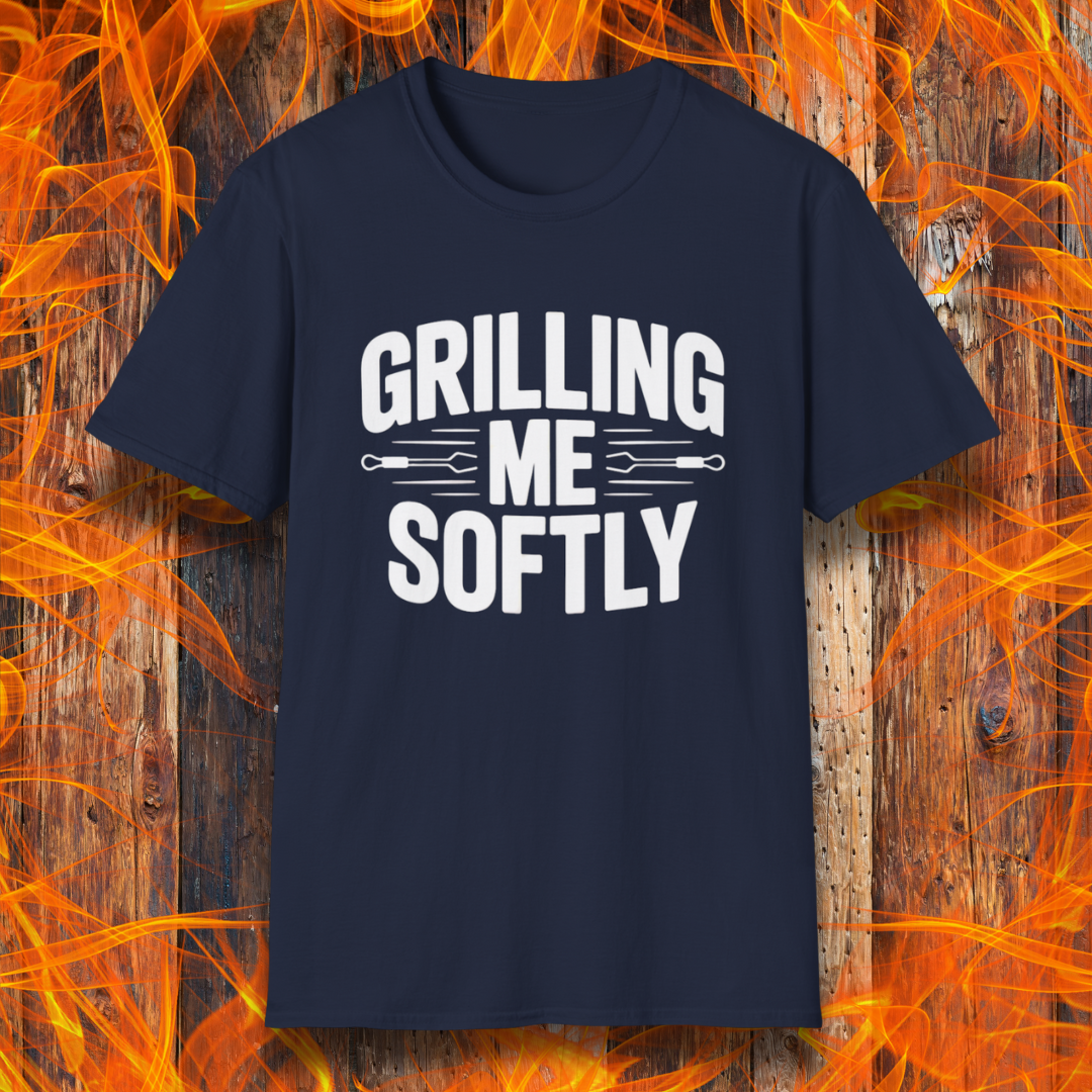 Navy T-shirt with bold white text that says "Grilling Me Softly," featuring BBQ tool graphics between the words — set against a wood and flame background, perfect for grill lovers with a sense of humor.