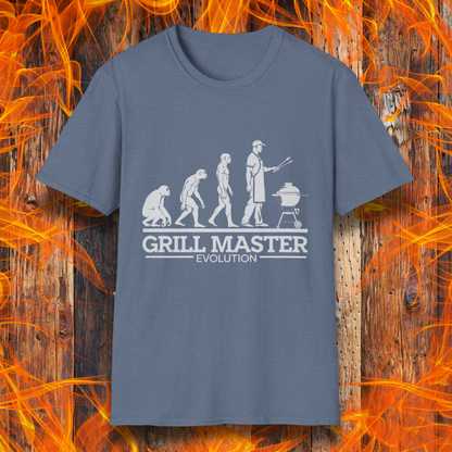 Heather Indigo T-shirt featuring a humorous "evolution" design that depicts the progression from primate to modern man, culminating in a grill master holding tongs in front of a BBQ grill. Below the illustration, bold white text reads "GRILL MASTER EVOLUTION," emphasizing the ultimate stage of human development—becoming a master of the grill.