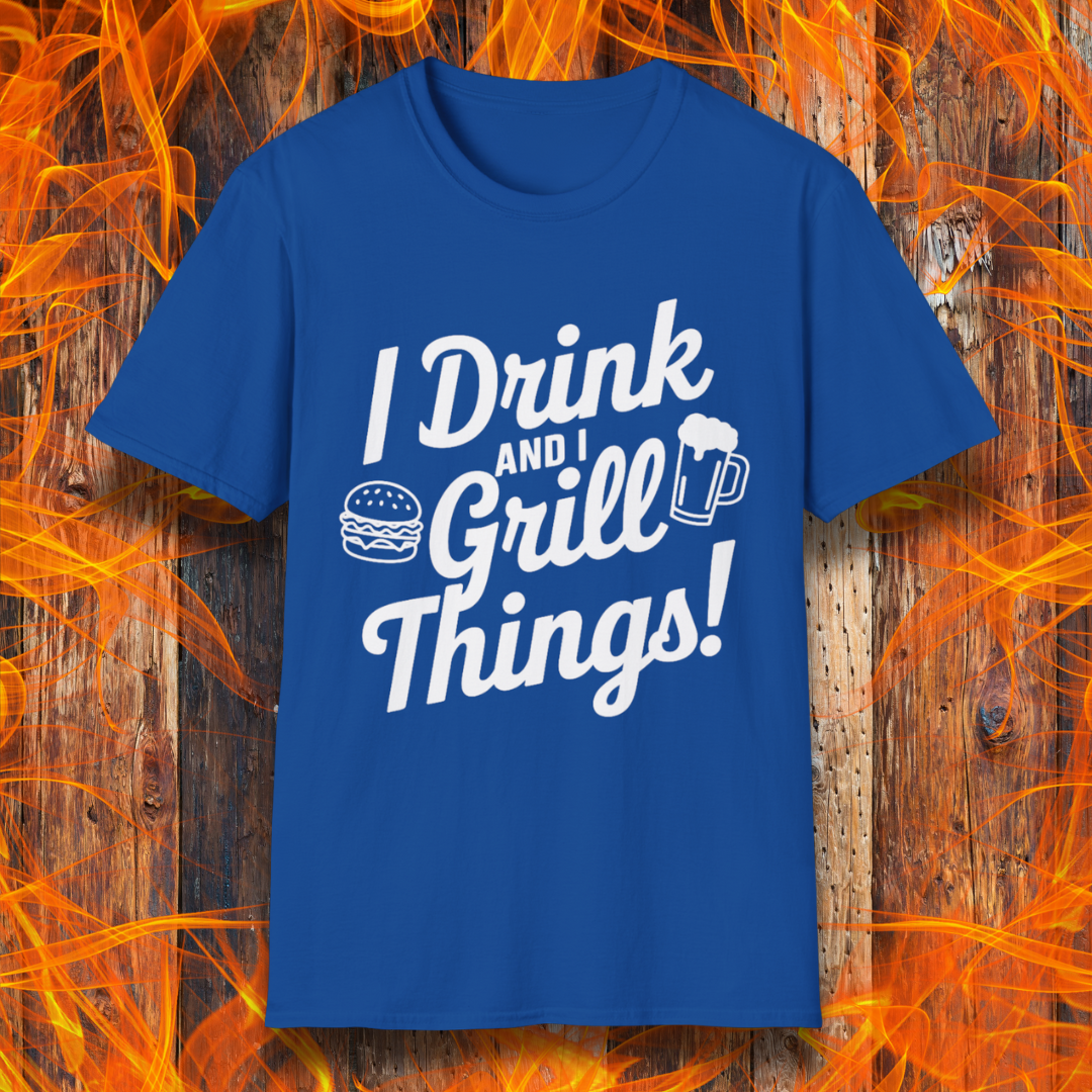 Royal Blue T-shirt featuring a bold, black text design that reads, "I Drink and I Grill Things!" in a playful, script-style font. The design includes small illustrations of a burger and a frothy beer mug, emphasizing a fun and laid-back grilling theme. The background showcases a rustic wooden surface with bright orange flames, enhancing the fiery BBQ aesthetic.