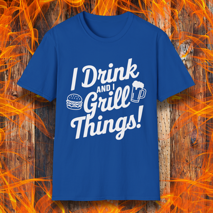 Royal Blue T-shirt featuring a bold, black text design that reads, "I Drink and I Grill Things!" in a playful, script-style font. The design includes small illustrations of a burger and a frothy beer mug, emphasizing a fun and laid-back grilling theme. The background showcases a rustic wooden surface with bright orange flames, enhancing the fiery BBQ aesthetic.