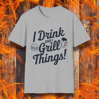 Sport Grey T-shirt featuring a bold, black text design that reads, "I Drink and I Grill Things!" in a playful, script-style font. The design includes small illustrations of a burger and a frothy beer mug, emphasizing a fun and laid-back grilling theme. The background showcases a rustic wooden surface with bright orange flames, enhancing the fiery BBQ aesthetic.