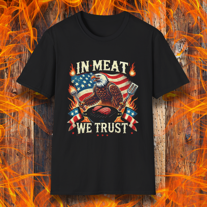 Black BBQ-themed T-shirt featuring a bold patriotic design with an American flag, a fierce bald eagle holding grilling utensils, flames, and the phrase 'In Meat We Trust' in vintage-style lettering.