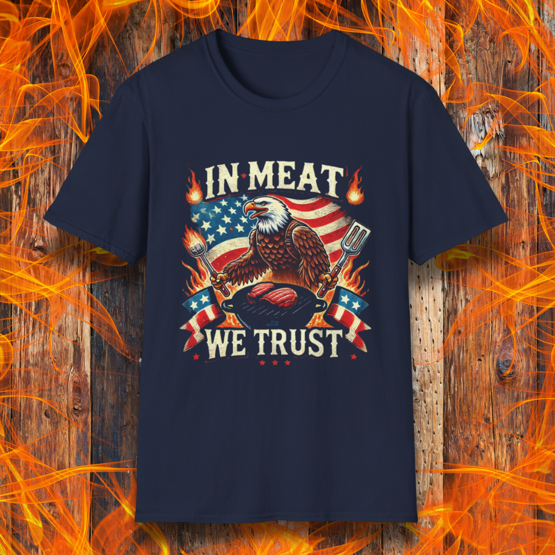Navy BBQ-themed T-shirt featuring a bold patriotic design with an American flag, a fierce bald eagle holding grilling utensils, flames, and the phrase 'In Meat We Trust' in vintage-style lettering.