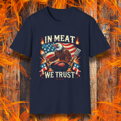 Navy BBQ-themed T-shirt featuring a bold patriotic design with an American flag, a fierce bald eagle holding grilling utensils, flames, and the phrase 'In Meat We Trust' in vintage-style lettering.