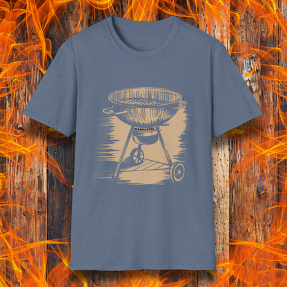 Heather Indigo T-shirt featuring a vintage-style beige sketch of a classic charcoal kettle grill. The illustration has a hand-drawn, rustic look with shading lines that add depth and texture. The background consists of a wooden surface with bright orange flames, enhancing the fiery BBQ theme.