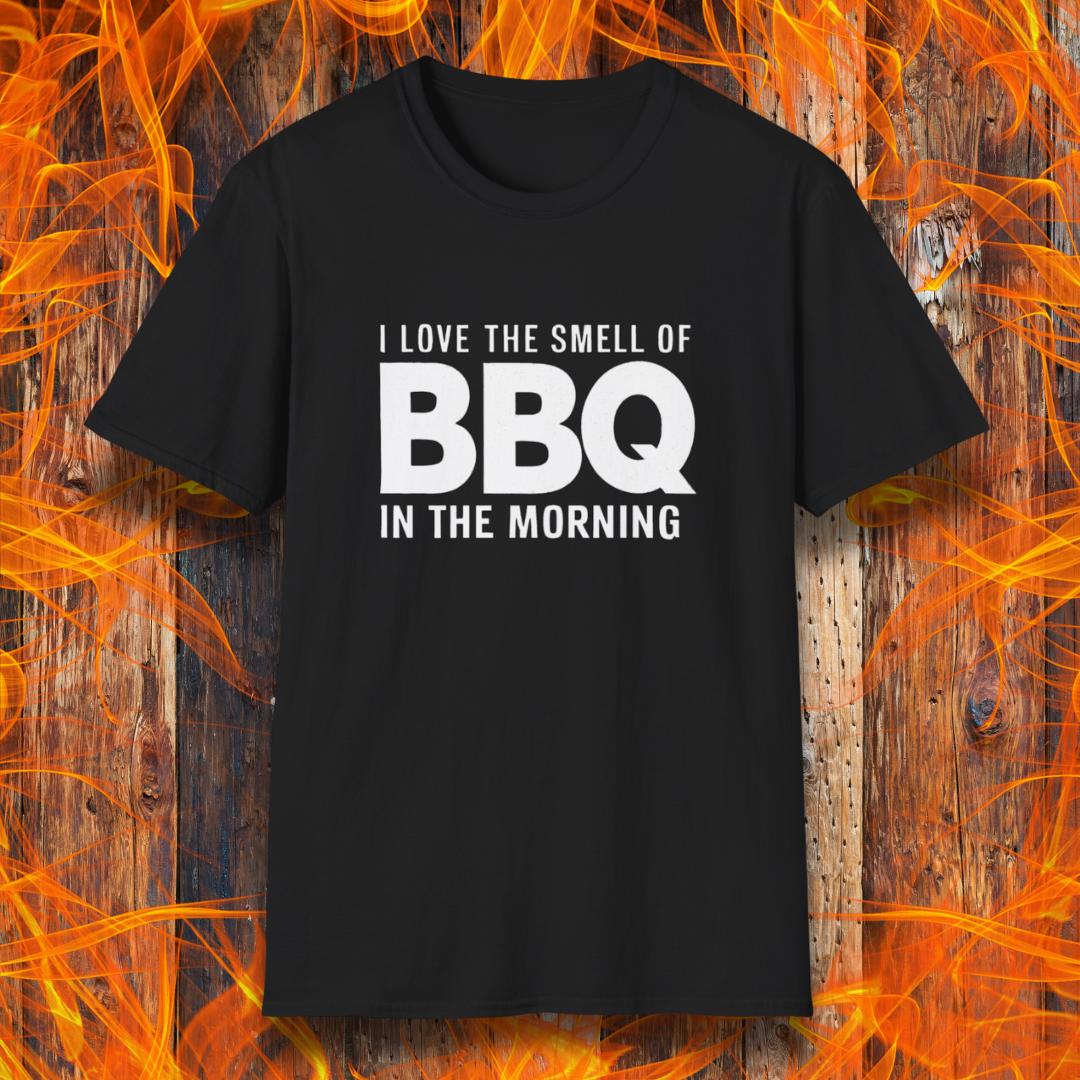 Black t-shirt with the phrase 'I Love the Smell of BBQ in the Morning' in bold white text, displayed against a fiery wooden background
