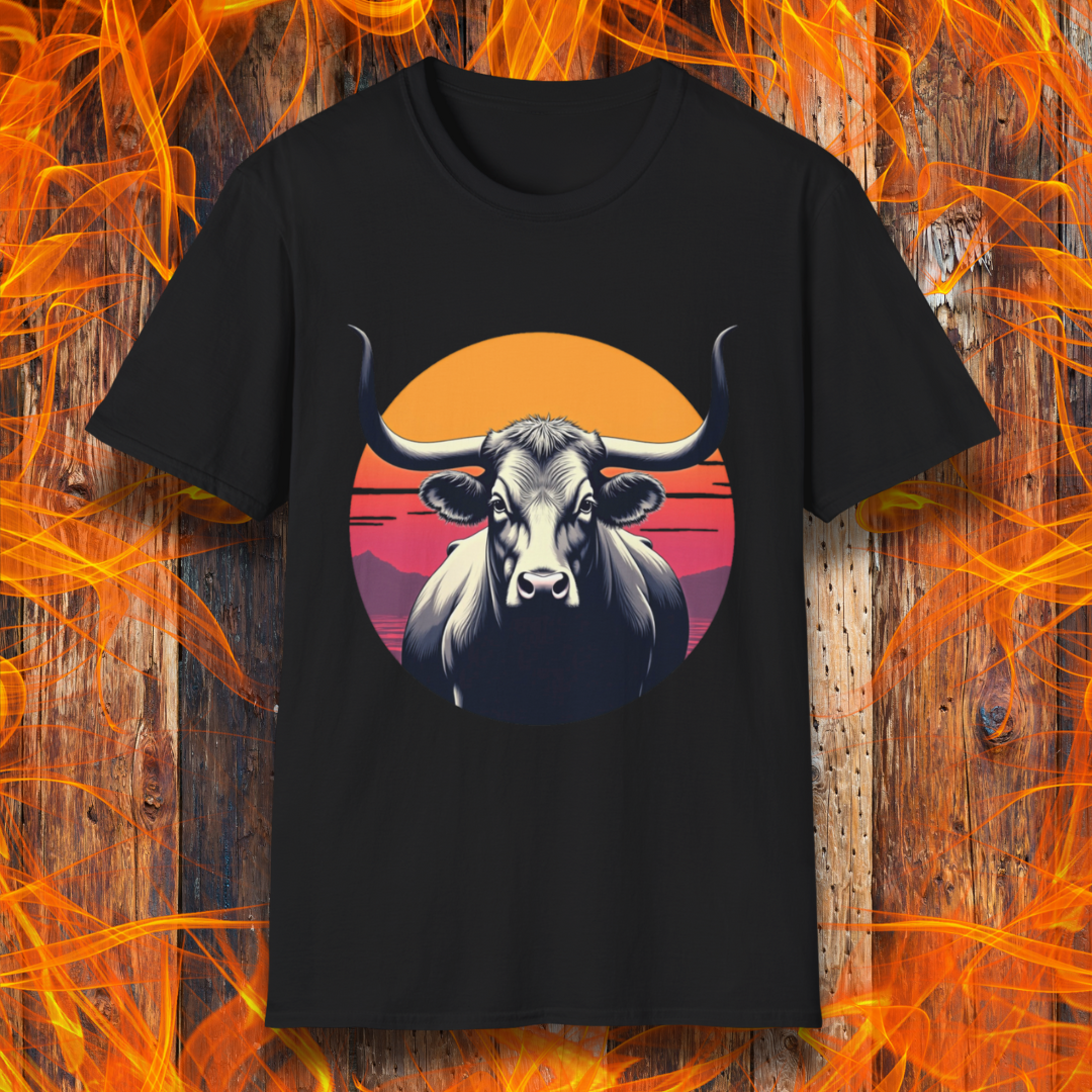 Black T-shirt featuring a striking design of a longhorn bull staring forward with an intense gaze. The bull is set against a circular backdrop of a sunset with warm orange, red, and pink hues, along with silhouetted mountains in the background. The design conveys strength, confidence, and a bold Western aesthetic, appealing to BBQ and cattle enthusiasts.