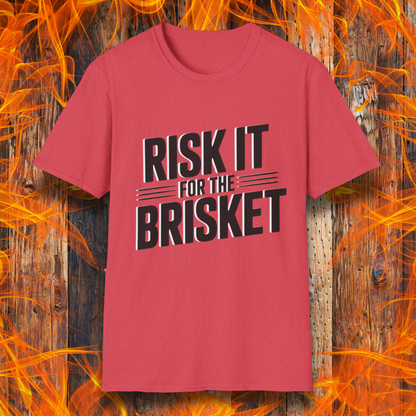 Red t-shirt with 'RISK IT FOR THE BRISKET' text on a wooden background with flames.