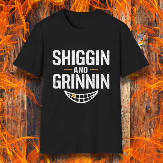  T-shirt featuring the phrase 'Shiggin and Grinnin' in bold, distressed white lettering. Below the text is a stylized smiling grill grate graphic. The design is set against a rustic wooden background with flames surrounding the edges, giving it a fiery barbecue-themed look.