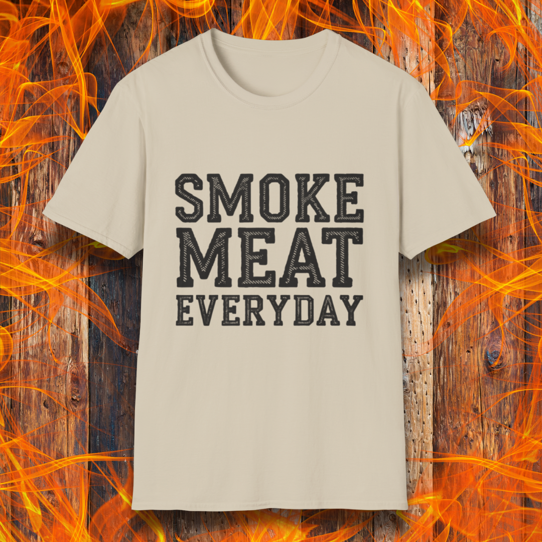 Sand T-shirt featuring bold, white, distressed-text lettering that reads "SMOKE MEAT EVERYDAY." The shirt is displayed against a fiery wooden background, reinforcing the BBQ and grilling theme.