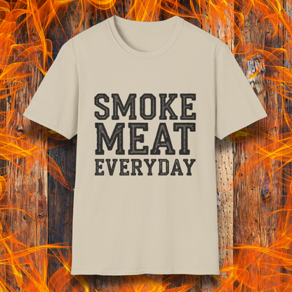 Sand T-shirt featuring bold, white, distressed-text lettering that reads "SMOKE MEAT EVERYDAY." The shirt is displayed against a fiery wooden background, reinforcing the BBQ and grilling theme.