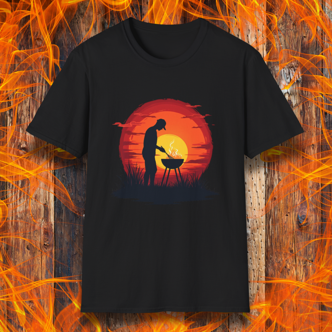 Black  T-shirt featuring a vibrant design of a silhouetted man grilling in front of a large, glowing sunset. The sunset has warm hues of red, orange, and yellow, creating a striking contrast against the dark background. The scene is framed with grass and subtle clouds, giving it an outdoorsy, serene BBQ vibe.