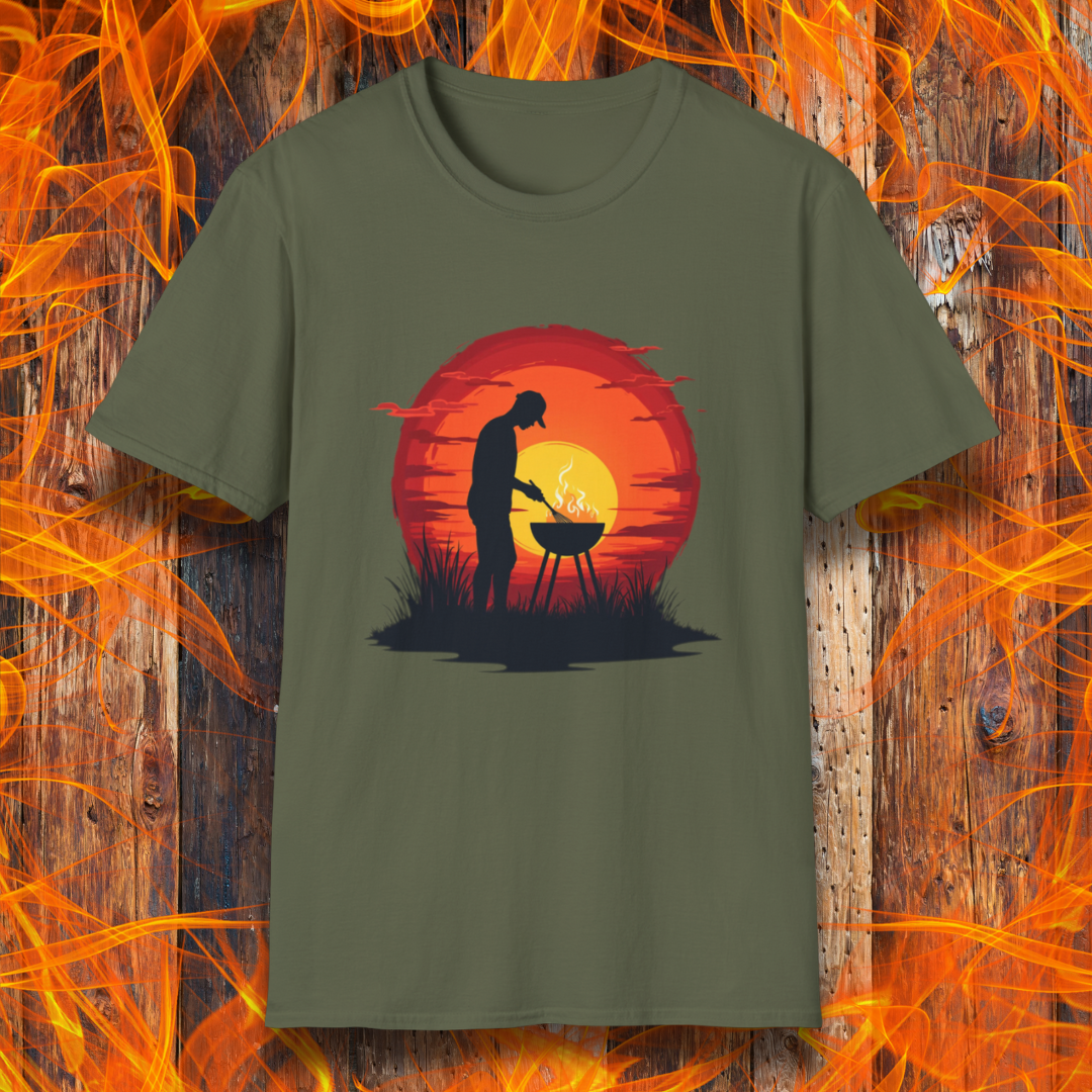 Military Green T-shirt featuring a vibrant design of a silhouetted man grilling in front of a large, glowing sunset. The sunset has warm hues of red, orange, and yellow, creating a striking contrast against the dark background. The scene is framed with grass and subtle clouds, giving it an outdoorsy, serene BBQ vibe.