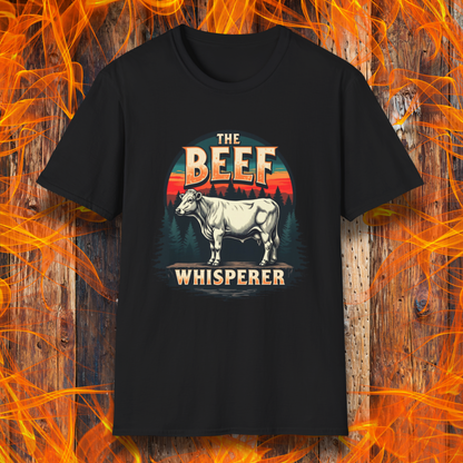 Black  T-shirt featuring a bold design with the words "The Beef Whisperer" in a vintage western-style font. Above the text, a detailed illustration of a cow stands on a patch of ground, framed by a scenic forest and a sunset with deep orange and red hues. The design has a rustic, outdoorsy feel, appealing to BBQ lovers and beef enthusiasts.