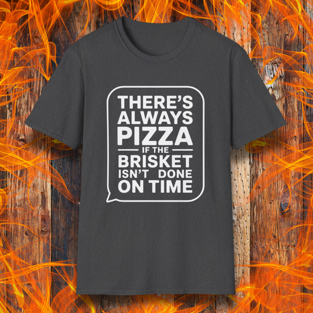 Dark Heather T-shirt featuring bold white text in a speech bubble that reads "There’s Always Pizza If the Brisket Isn’t Done on Time," displayed over a wooden background with flames — a humorous shirt for BBQ fans who know the struggle of low-and-slow cooking.