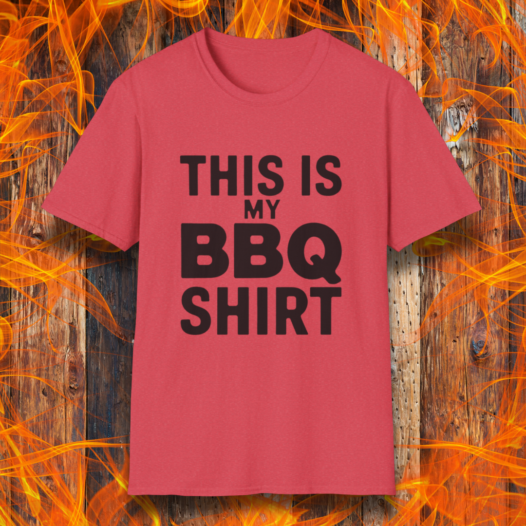 Heather Red T-shirt with bold black text that reads "THIS IS MY BBQ SHIRT." The shirt is displayed against a fiery wooden background, reinforcing its BBQ and grilling theme.
