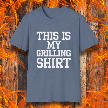 Heather Indigo T-shirt with bold white text that reads "THIS IS MY GRILLING SHIRT." The shirt is displayed against a fiery wooden background, emphasizing its BBQ and grilling theme.