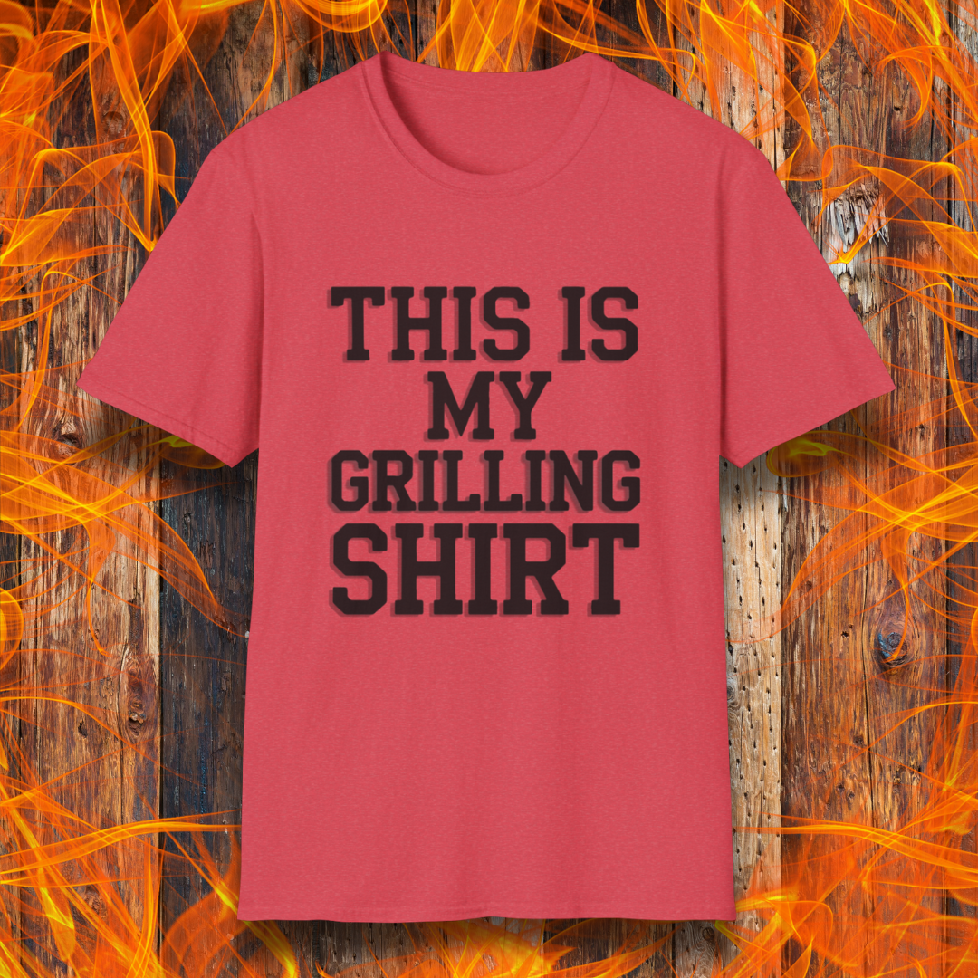 Heather Red T-shirt with bold black text that reads "THIS IS MY GRILLING SHIRT." The shirt is displayed against a fiery wooden background, emphasizing its BBQ and grilling theme.