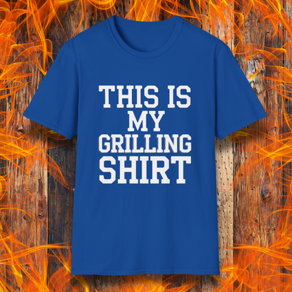 Royal Blue T-shirt with bold white text that reads "THIS IS MY GRILLING SHIRT." The shirt is displayed against a fiery wooden background, emphasizing its BBQ and grilling theme.