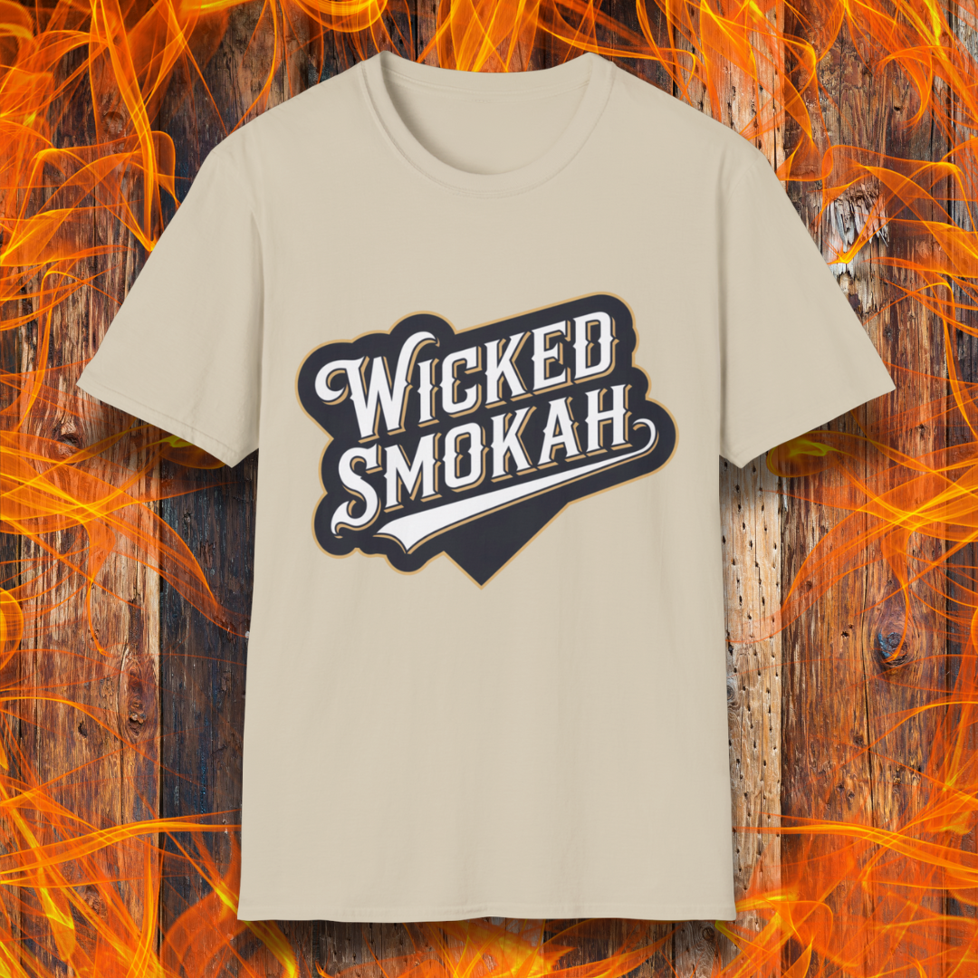 Sand T-shirt featuring a bold, vintage-style design that reads "Wicked Smokah" in stylized typography, resembling a sports team logo. The lettering has a mix of white and gold outlines, giving it a classic and rugged look. The shirt is displayed against a fiery wooden background, reinforcing the smoky BBQ theme.